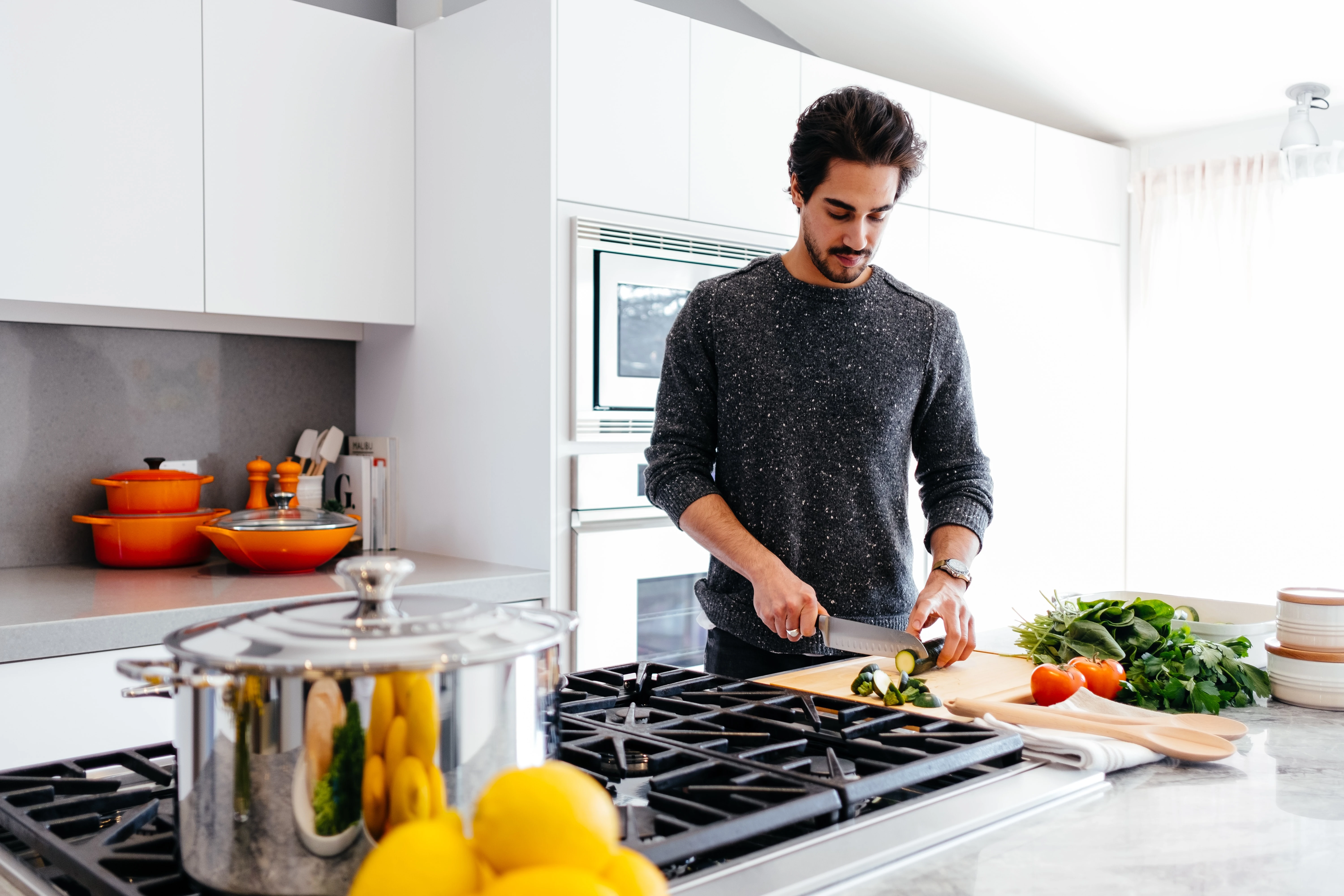 Homme qui cuisine dans une cuisine. Il découpe des légumes avec un couteau sur une planche à découper